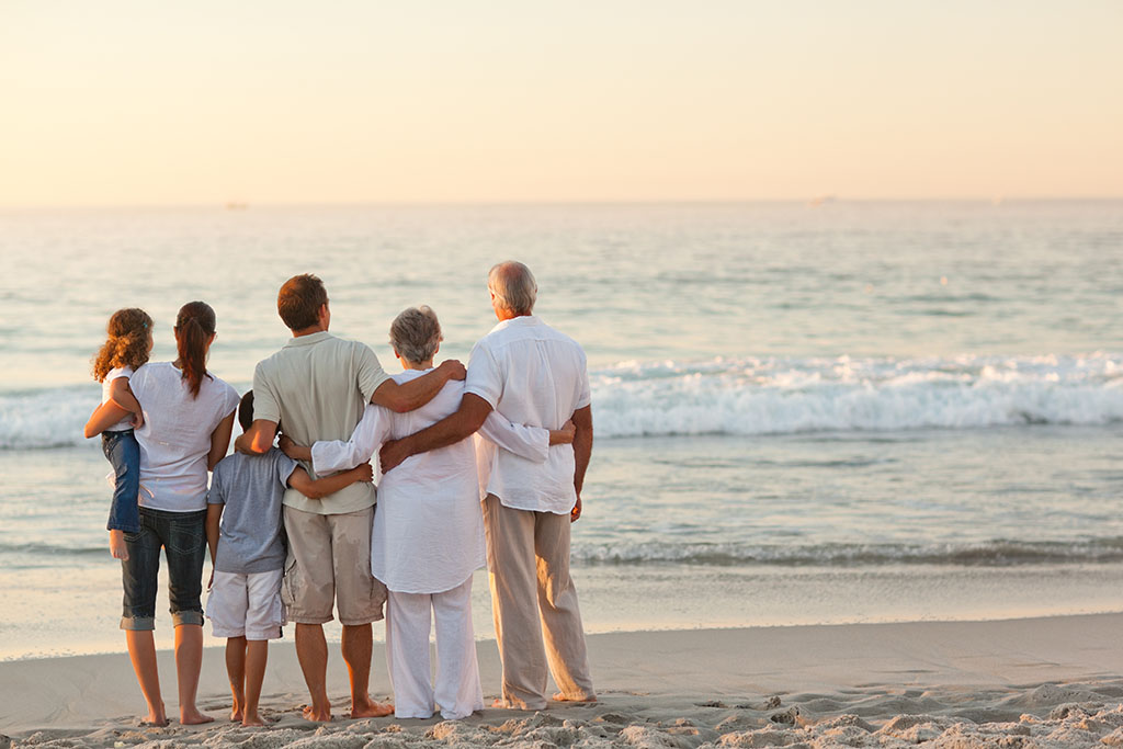 three generations of family hugging on the beach